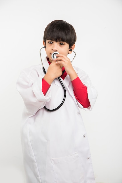 Happy little Indian asian boy in medical uniform as a doctor, holding stethoscope and looking at camera isolated on white background