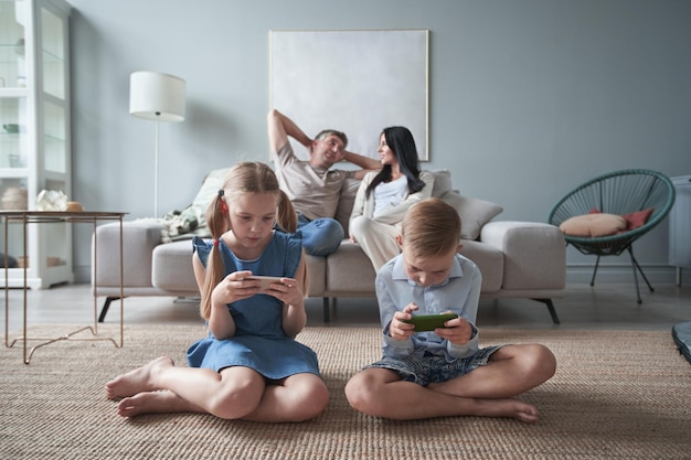 Happy little kids brother and sister use phones at home