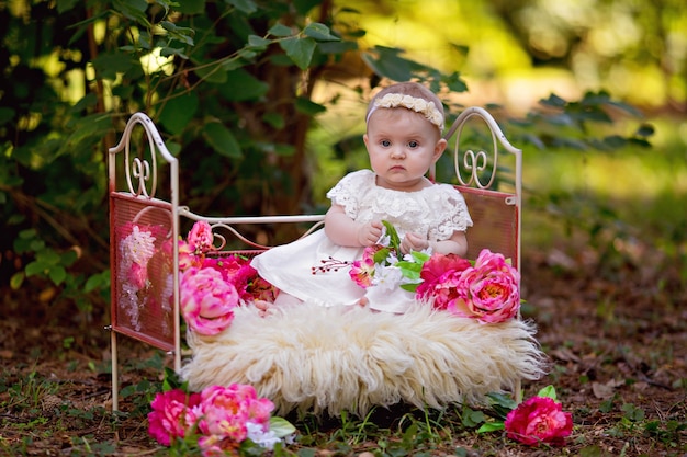 Happy little princess baby girl in bed with pink flowers outdoors in summer.