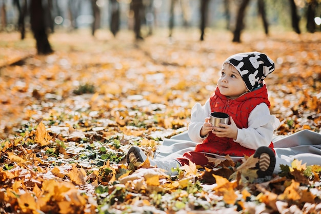 Happy little toddler baby daughter with red thermos and cup in autumn picnic in fall nature