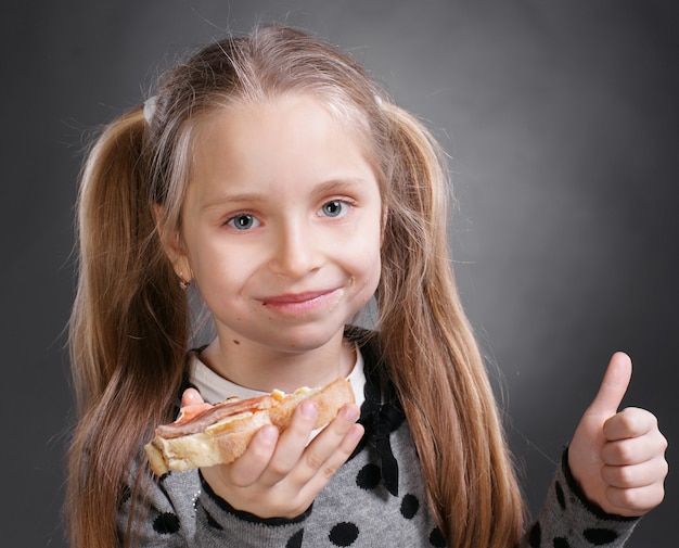 Happy little woman eating bread and butter with fish and showing yes sign