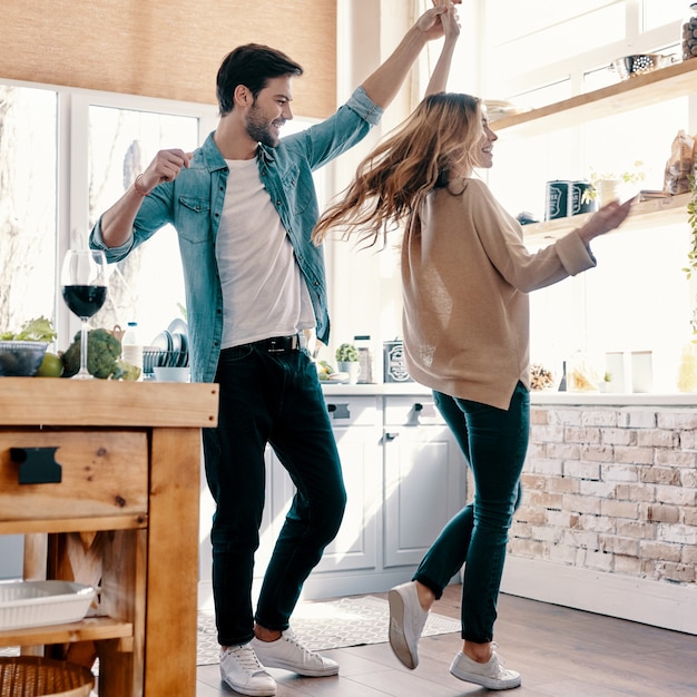 Happy and in love. Full length of beautiful young couple in casual clothing dancing and smiling while standing in the kitchen at home