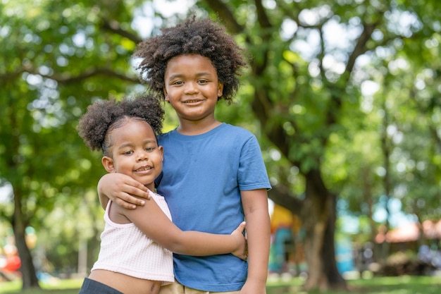 Happy lovely kids African American boy and little girl smiling and hugging together in park