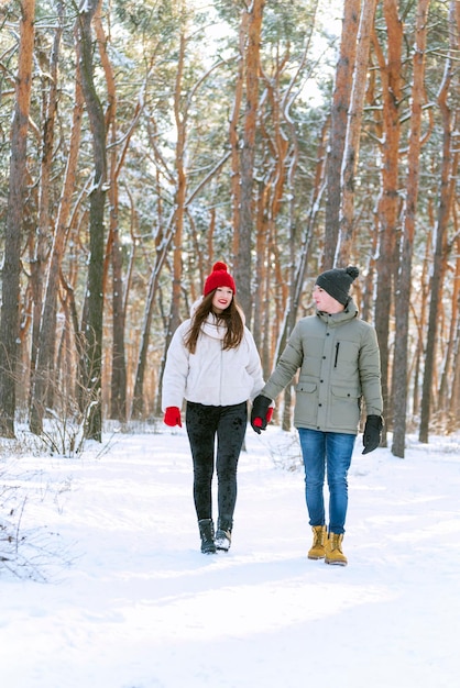 Happy lovers walk in snowy park. Young couple walks in winter through the forest and holds hands. Vertical frame.