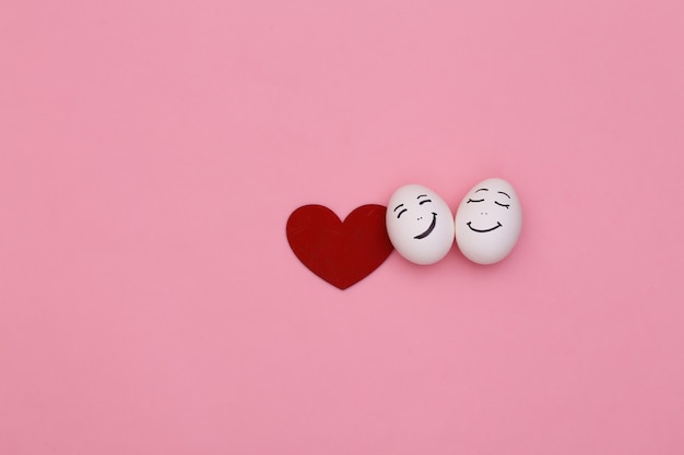 Happy loving couple of chicken eggs faces and heart on pink background