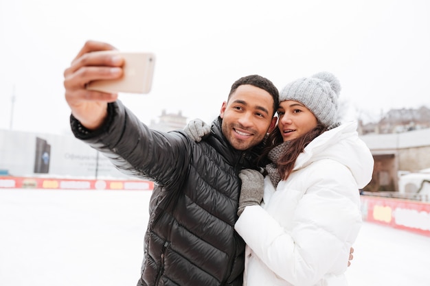 Happy loving couple skating at ice rink outdoors. Make selfie.