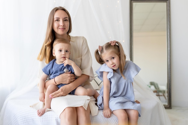 Happy loving family Mother with daughter and newborn son are sitting on the bed in the bedroom interior in pastel colors