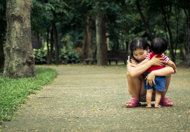 Happy loving mother and girl cuddling outdoor summer background.