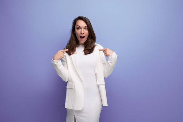 Happy lucky brunette woman in ivory jacket and white dress on purple background with copy space