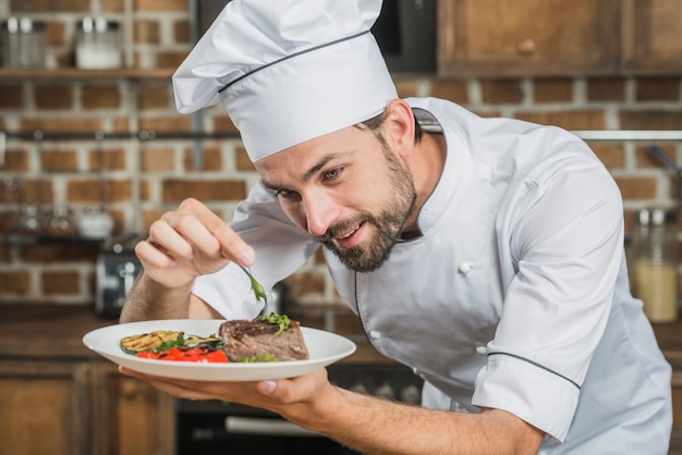 Happy male chef preparing beef steak with vegetable decoration