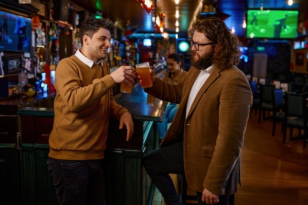 Happy male friends clinking with beer mugs in pub