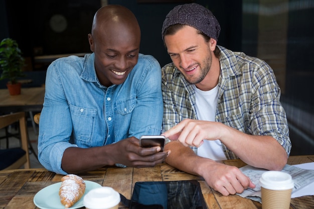 Happy male friends using mobile phone at table in coffee house