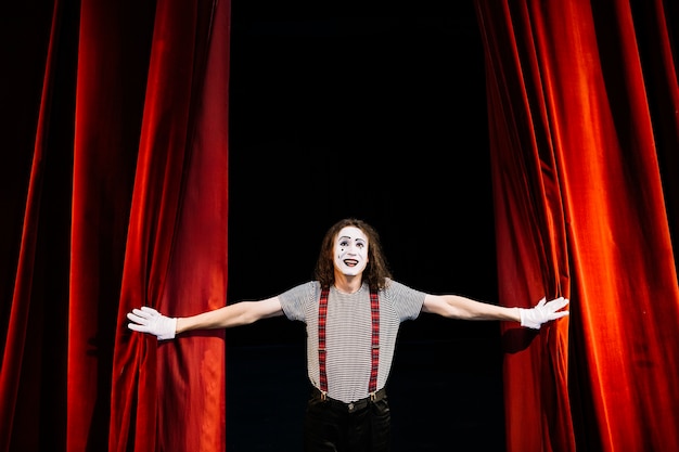 Happy male mime artist near red curtain