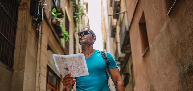 Happy male tourist maps user walking in old town alley an using a map Barcelona Spain