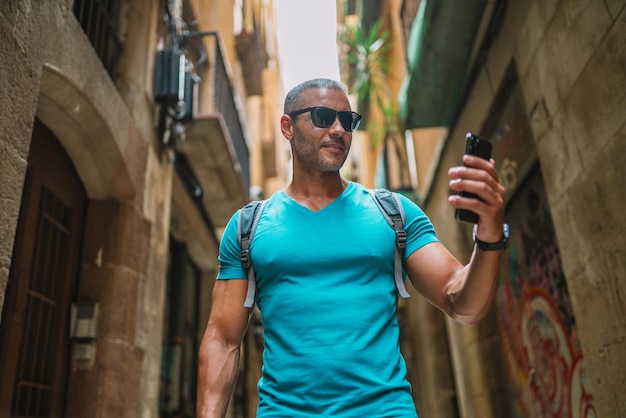 Happy male tourist phone user walking in old town alley an using smartphone GPS maps concept