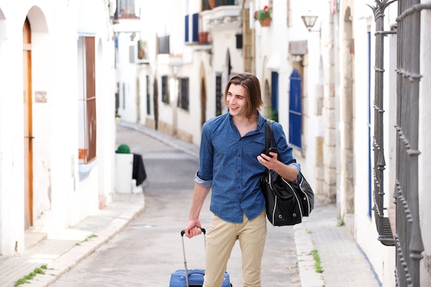 Happy man in city street with smart phone and luggage