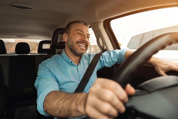 Happy man in earphones enjoying music driving luxury car