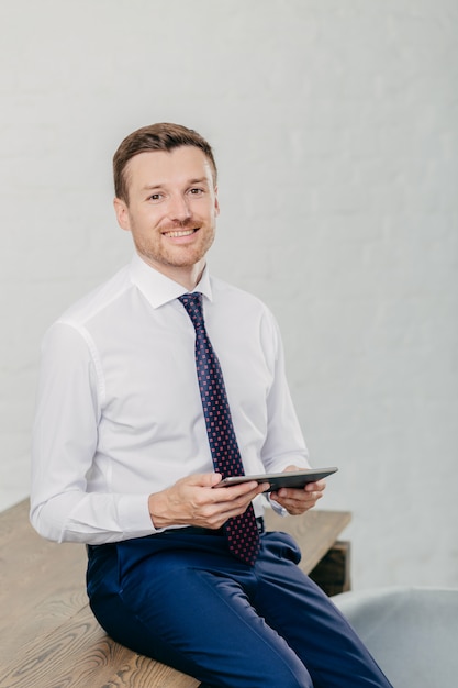 Happy man in formal clothes checks email and reads notification on modern tablet computer