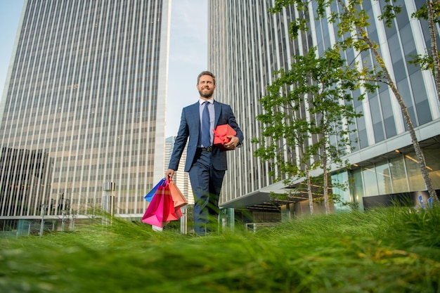 Happy man in formalwear hold shopping bags and present box walk outside the office occasion