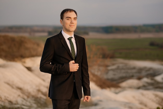 Happy man, groom in elegant suit coat outdoors on natural background. Stylish groom waiting the bride. wedding emotional portrait of the groom outdoor at sunset