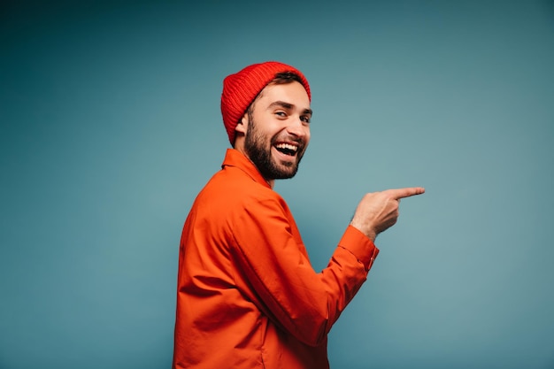 Happy man in hat and orange jacket looks into camera and points fingers to right