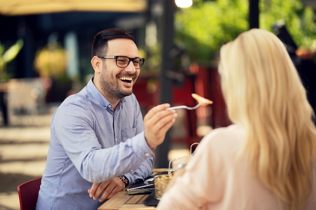 Happy man having lunch with his girlfriend and feeding her in a restaurant