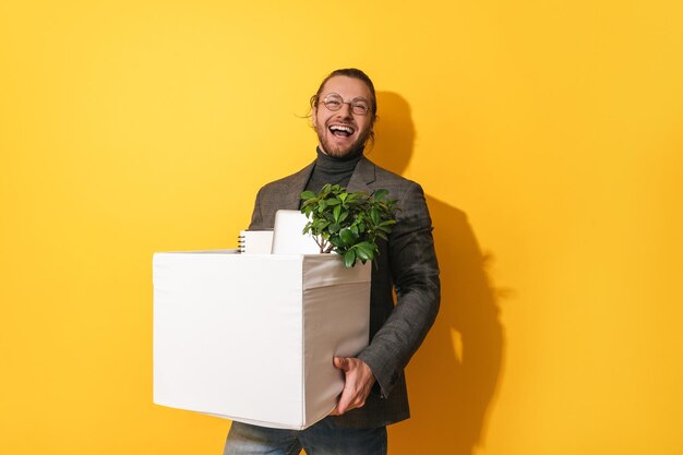 Happy man holding box with personal items after job promotion against yellow background