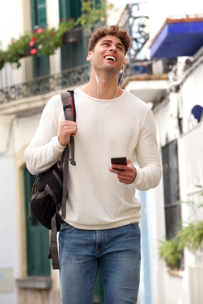 Happy man holding cellphone with backpack and earphones