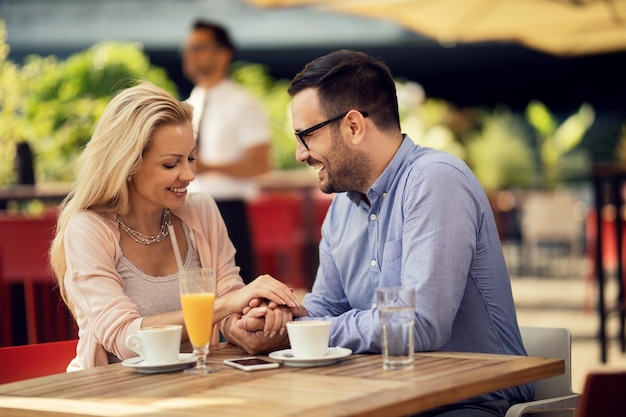 Happy man holding hands with his girlfriend and talking to her while being on a date in a cafe