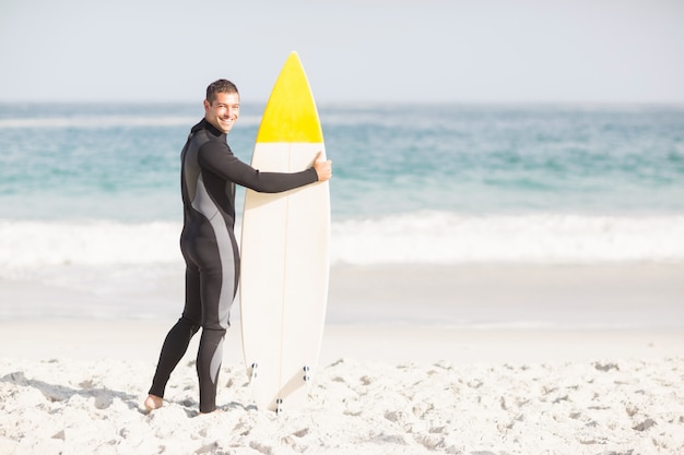 Happy man holding a surfboard on the beach