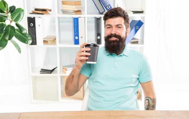 Happy man holding takeaway coffee cup sitting in office coffee break