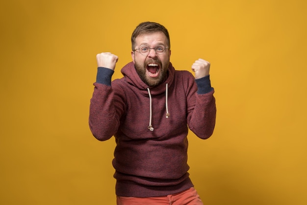 Happy man makes a winner gesture he energetically raises fists up and shouts in joy