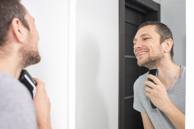 A happy man shaves and looks in the mirror