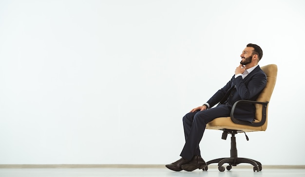 The happy man sitting on an office chair on the white wall background