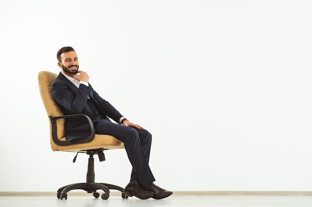 The happy man sitting on an office chair on the white wall background