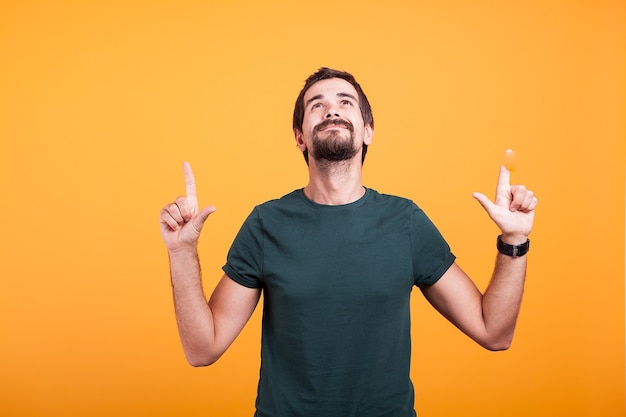 Happy man smiling and pointing up with his fingers. Copyspace available for your text and advertisement promotion. Shot on orange background