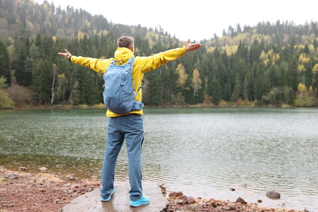 Happy man spreads hands to sides enjoying wild nature while hiking tourist with backpack stands