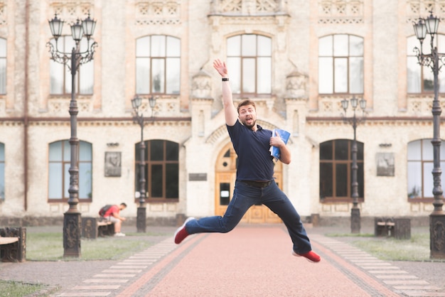 Happy man student with books in his hands jumping against the background of the university building.