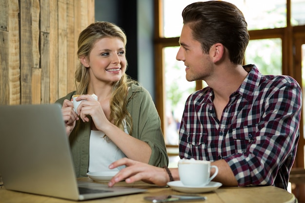 Happy man using laptop while looking at woman in coffee shop