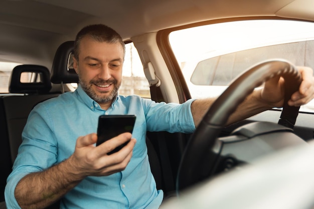 Happy man using smartphone while driving car