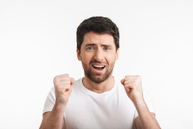 happy man with bristle in casual t-shirt rejoicing and clenching fists isolated over white wall