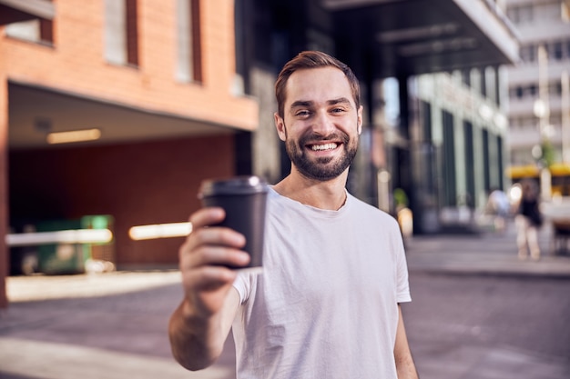 Happy man with coffee smiles outdoors close up