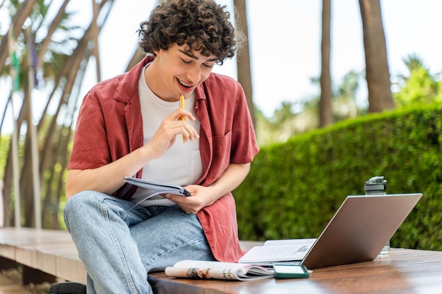 Happy man with curly hair writing some notices on paper document and preparing for exam