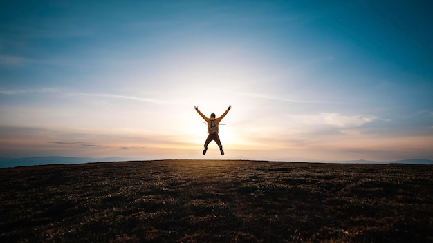 Happy man with open arms jumping on the top of mountain