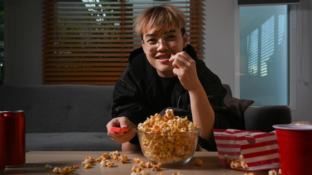 Happy man with remote control eating popcorn and watching movie at night Entertainment and leisure activity concept