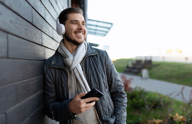 Happy man with a wide smile listens to music in headphones on a mobile phone leaning against the