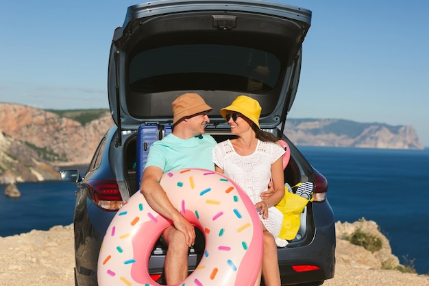 Happy man and a woman are sitting in the trunk of a car near the sea