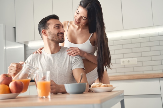 Happy man and woman eating morning breakfast together. Young woman gently hugging shoulders of her husband