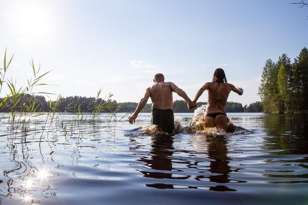 Happy man and woman hold hands run and bathe in a clean forest lake