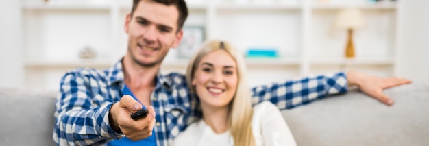 The happy man and woman sit on the sofa and hold the remote control